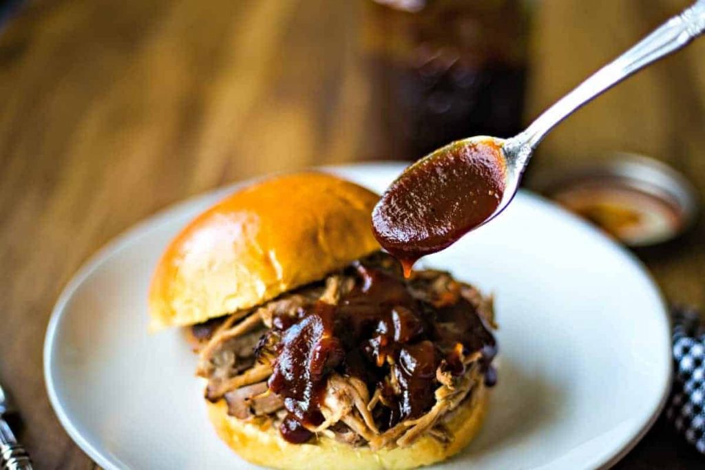 A plate of food and a spoon on a table, with Barbecue sauce and pulled pork