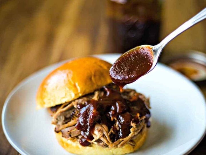 A plate of food and a spoon on a table, with Barbecue sauce and pulled pork