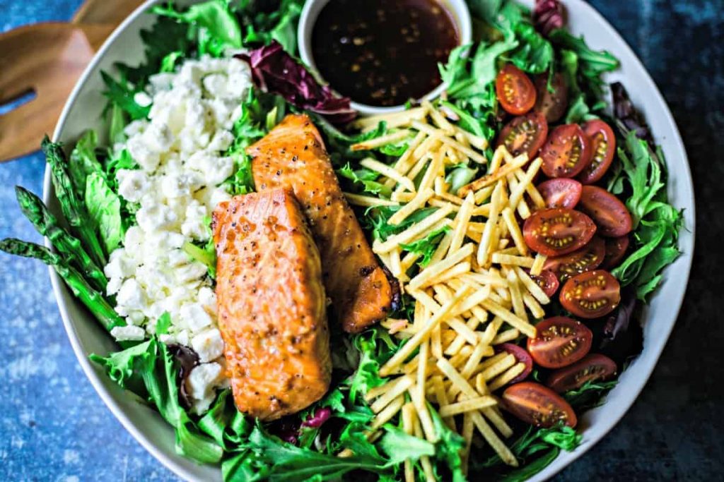 close up of feta cheese, salmon, potato sticks, and sliced tomatoes on a salad