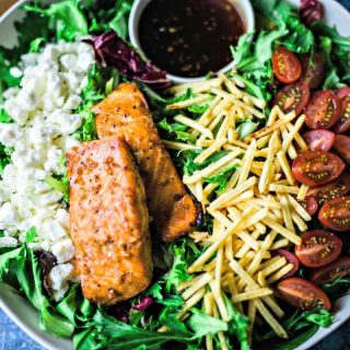 close up of feta cheese, salmon, potato sticks, and sliced tomatoes on a salad