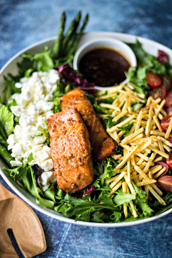 grilled salmon on salad greens in a white bowl on a blue background