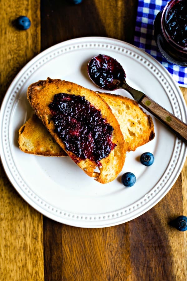 sourdough toast with a smear of blueberry jam on a white plate with a wooden spoon