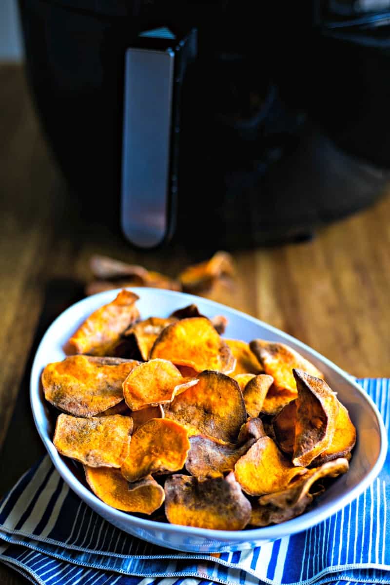 sweet potato chips in a white bowl in front of an air fryer