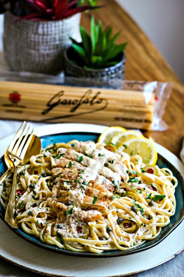 a blue plate with lemon chicken scallopini, lemon slices, and gold silverware