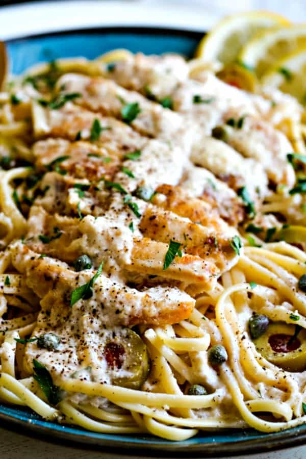 close up shot of slices of chicken and lemon sauce on a plate of pasta