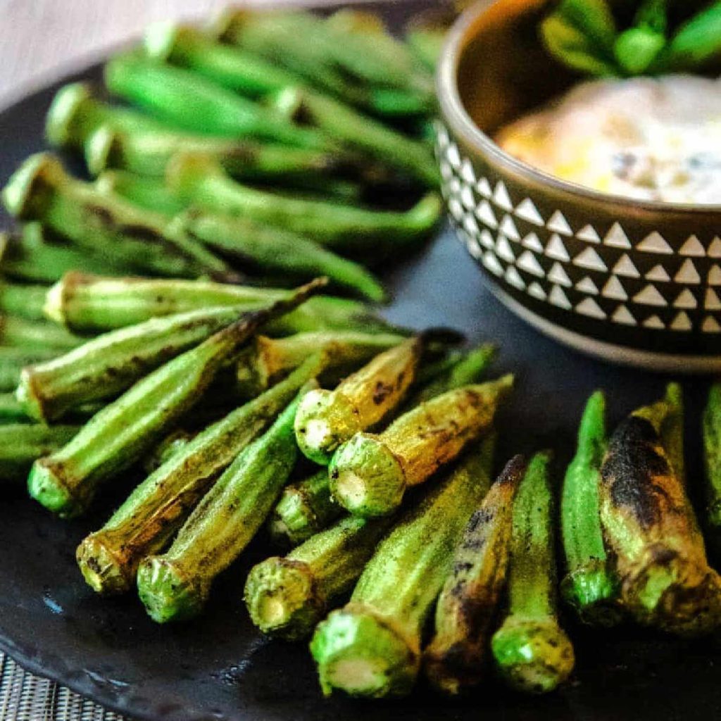 Grilled okra on a platter with a bowl of dipping sauce on a table.