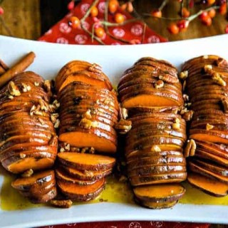 a white platter with four hasselback sweet potatoes drizzled in melted butter and pecans
