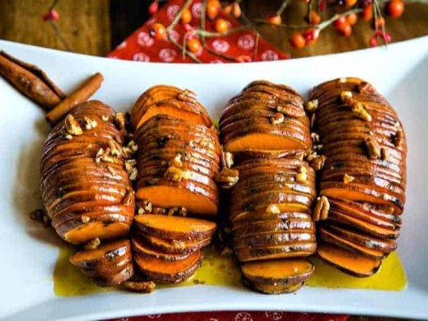 a white platter with four hasselback sweet potatoes drizzled in melted butter and pecans