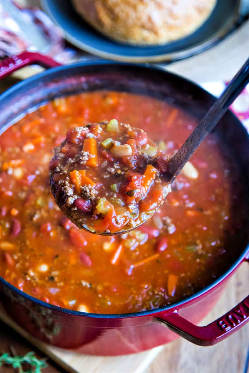 a ladle lifting Pasta e Fagioli Soup out of a  a Dutch oven