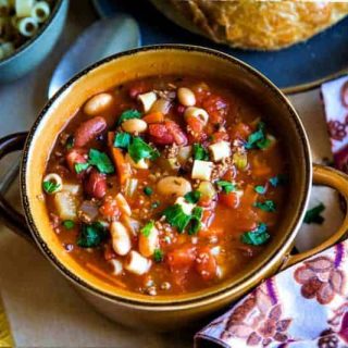 earthenware bowl of Pasta e Fagioli Soup on a dinner table with paisley napkin and crusty loaf of bread