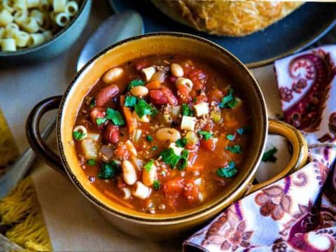 earthenware bowl of Pasta e Fagioli Soup on a dinner table with paisley napkin and crusty loaf of bread