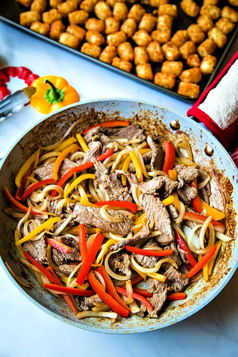 A frying pan full of food, with Cheesesteak and peppers