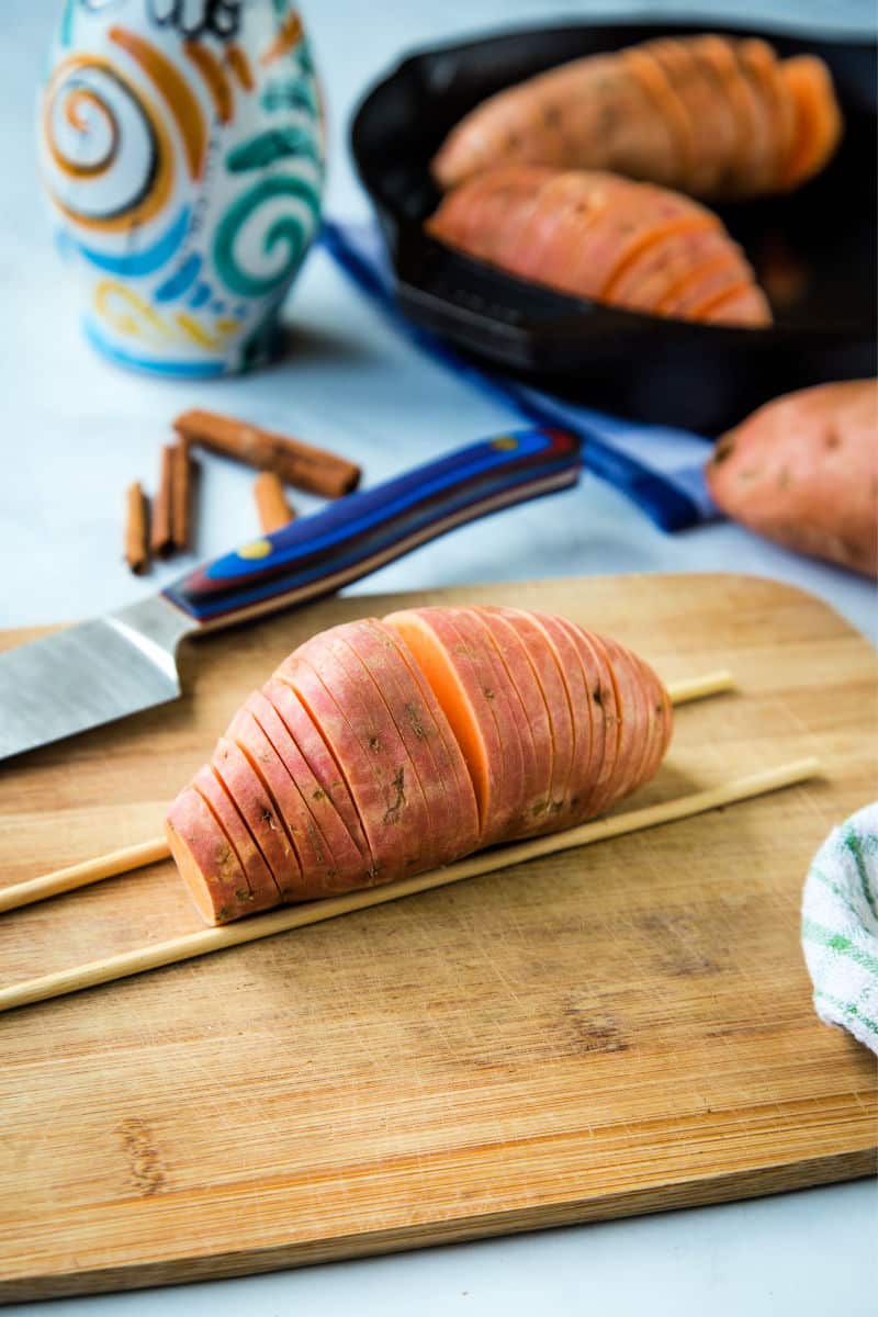 sliced sweet potato on a cutting board with chop sticks as a guide to make them hasselback