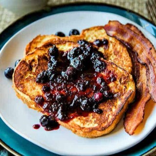 two slices of french toast on a white plate with bacon and berry preserves