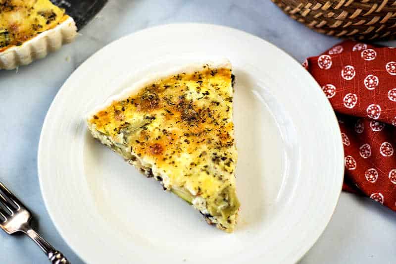 a slice of quiche on a white plate with a fork and red napkin
