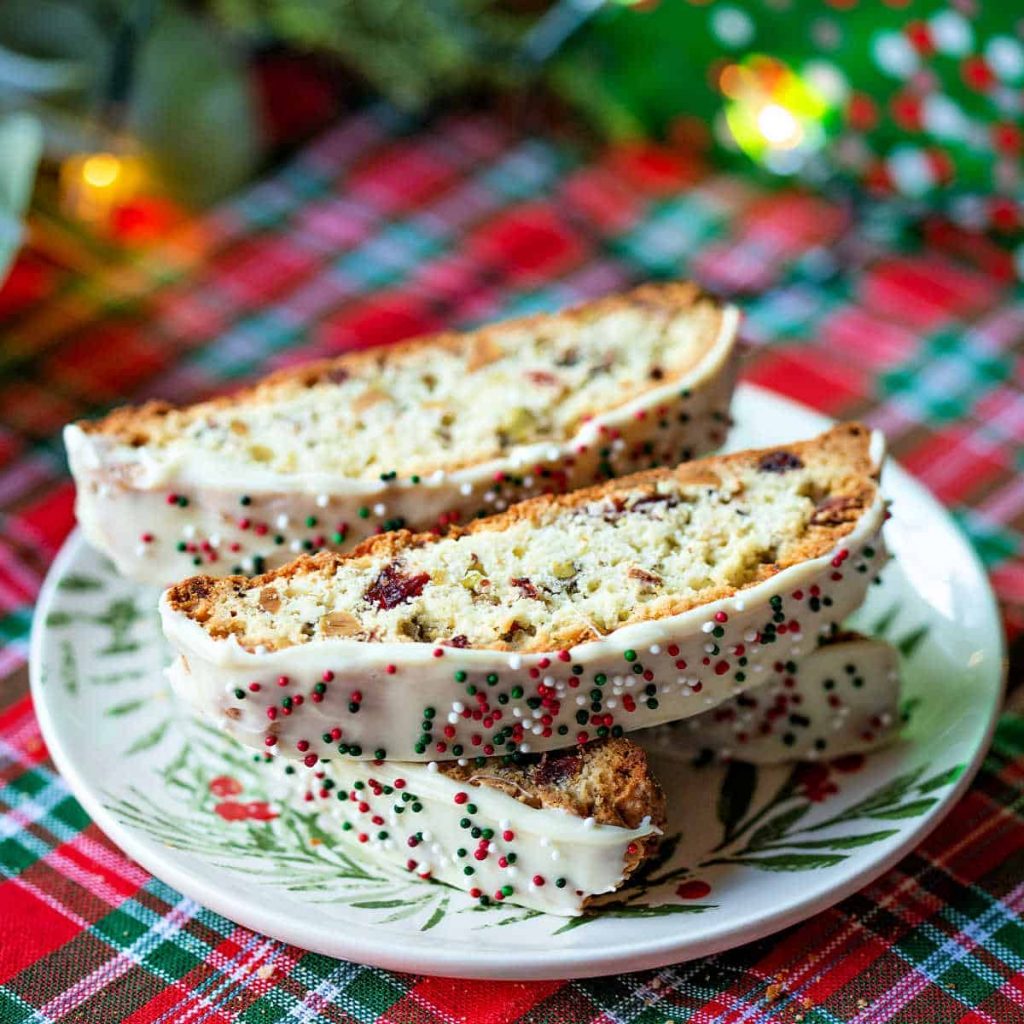 pieces of cranberry pistachio biscotti on a Christmas plate setting on a red and green plaid table cloth