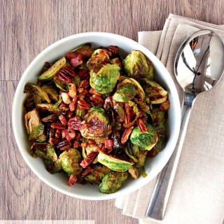 A bowl of Brussels sprouts wth pancetta and pecans on a wooden background with a serving spoon