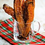 strips of candied bacon in a glass mug sitting on a christmas tablecloth.