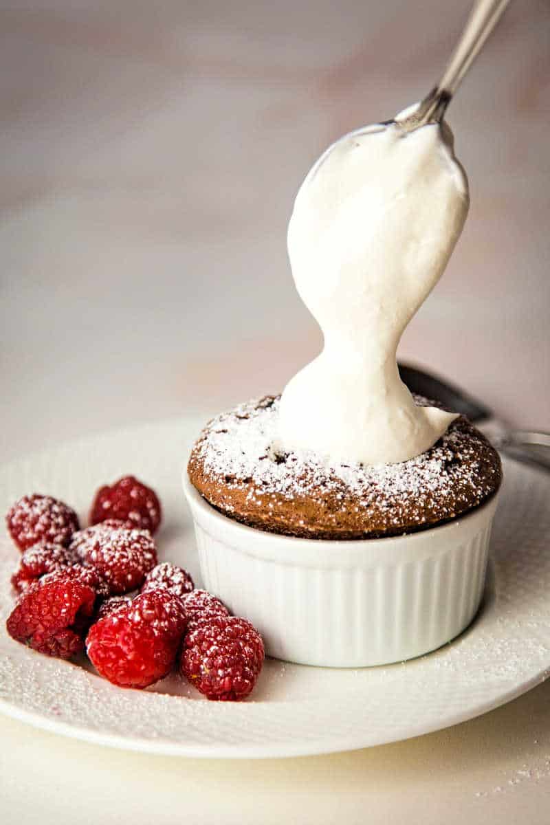 spooning whipped cream on top of chocolate souffle