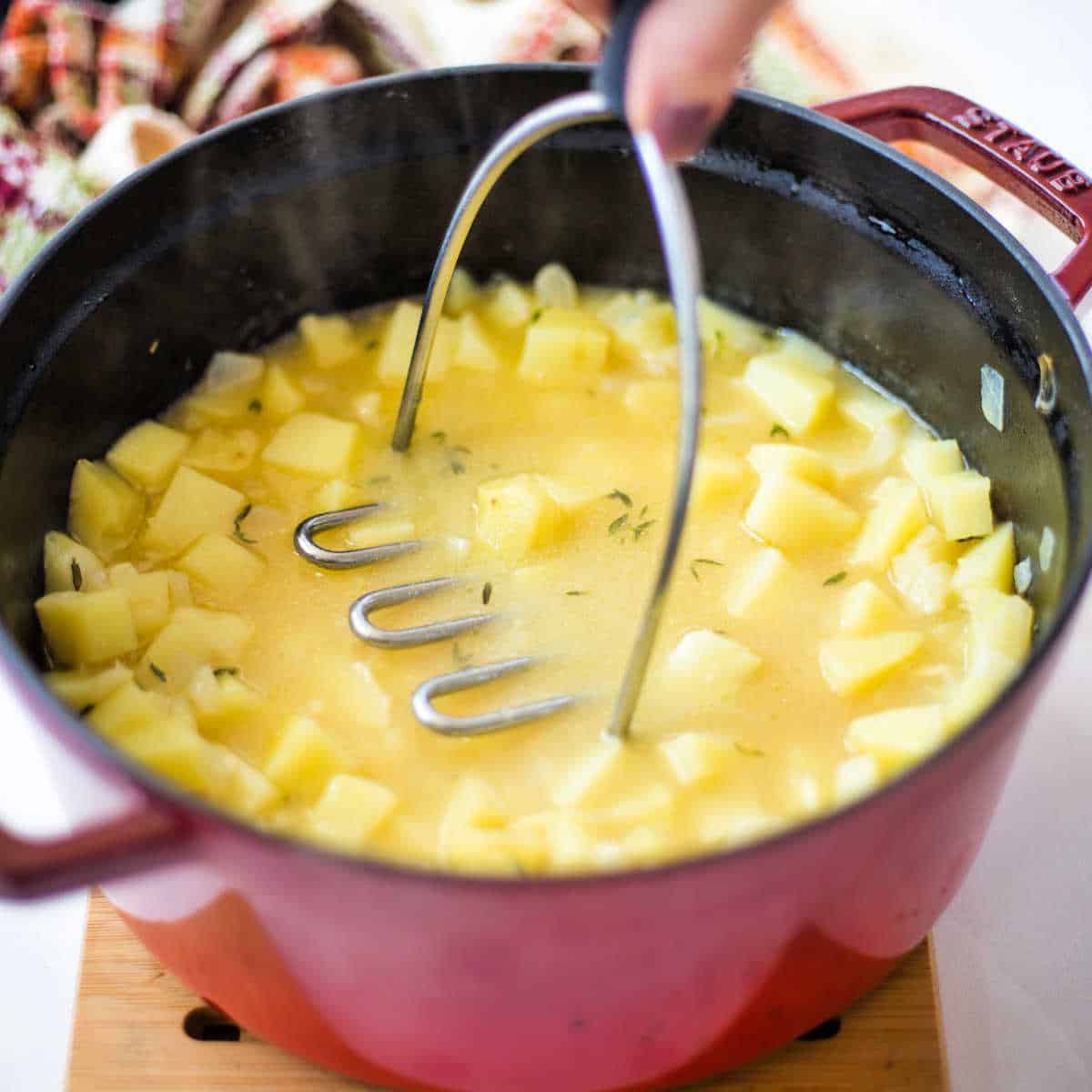 old fashioned potato soup in a soup pot with a potato masher