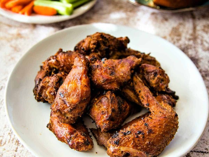 a plate of smoked chicken wings with carrots and celery in the background