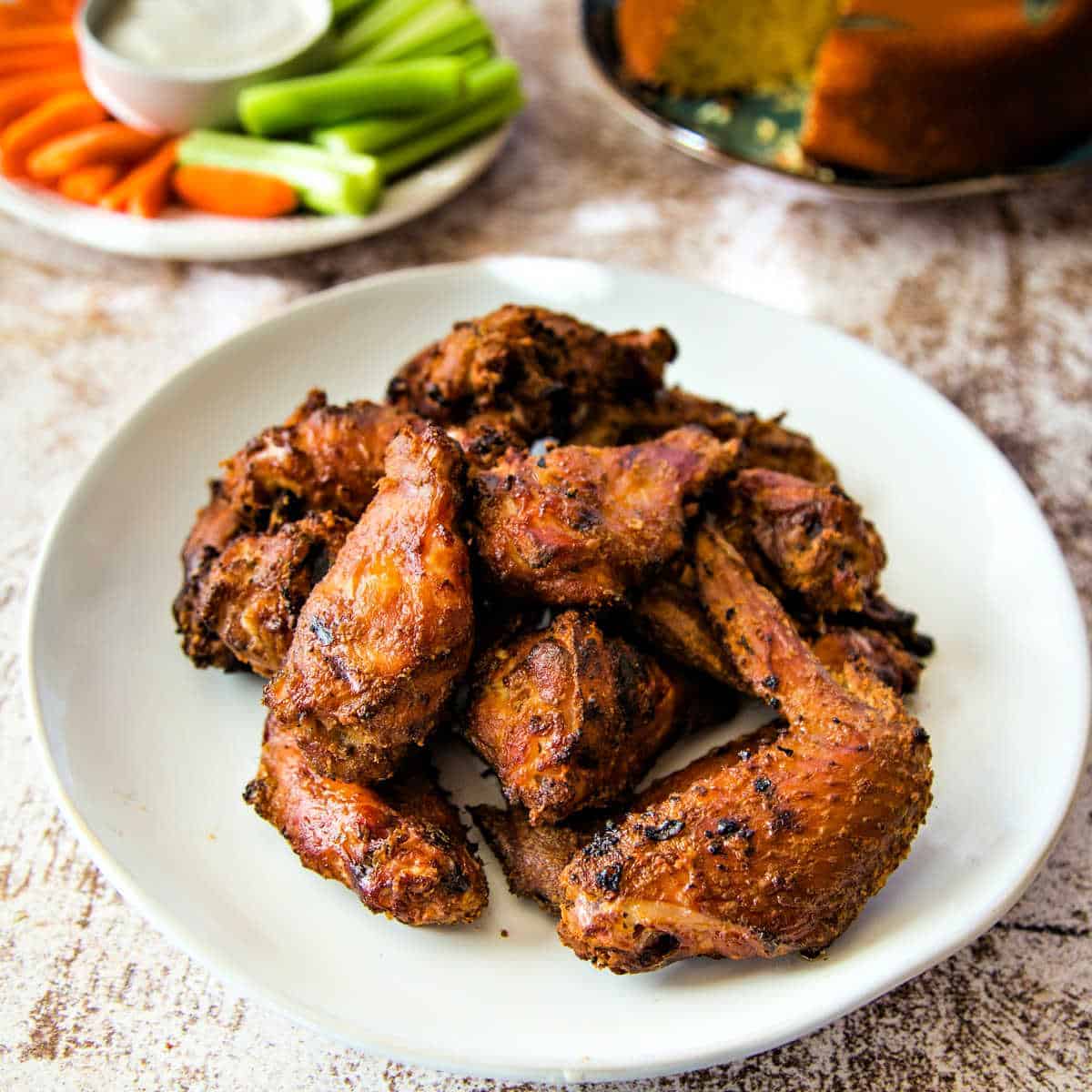 a plate of smoked chicken wings with carrots and celery in the background