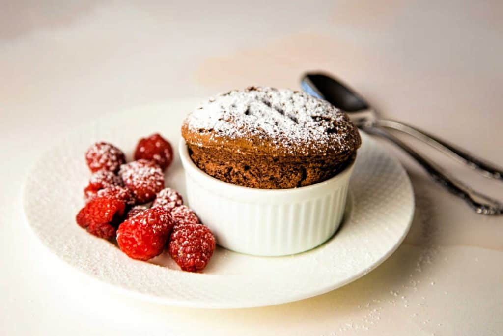chocolate souffle dusted with powdered sugar on a white plate with fresh raspberries