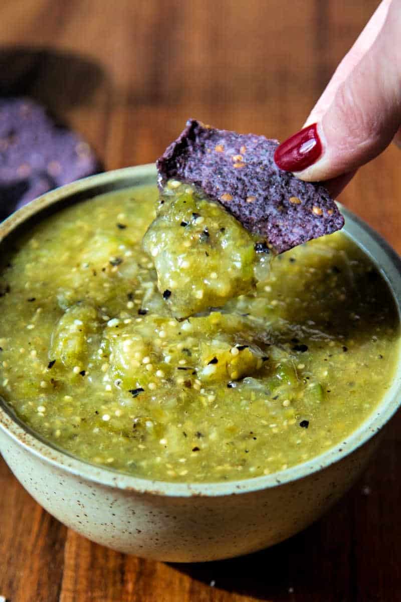 dipping a blue corn tortilla in a bowl of roasted tomatillo salsa