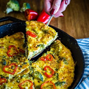 lifting a slice of broccoli frittata out of a cast iron sillet