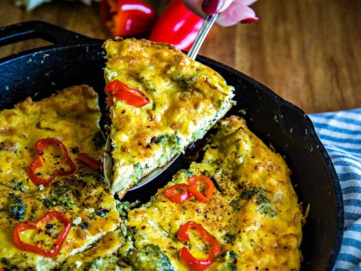 lifting a slice of broccoli frittata out of a cast iron sillet