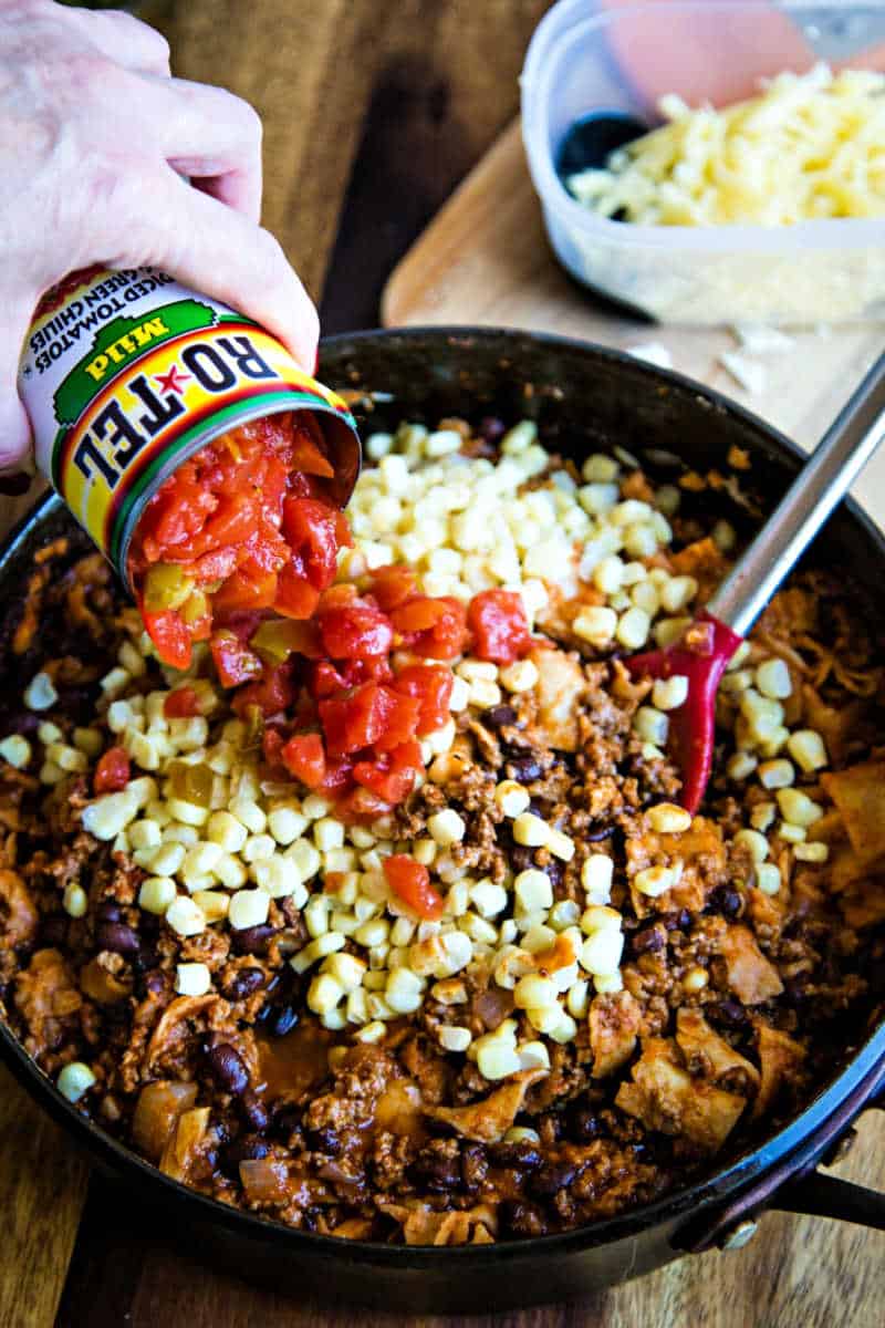 adding a can of diced tomatoes and green chilies to beef enchilada skillet