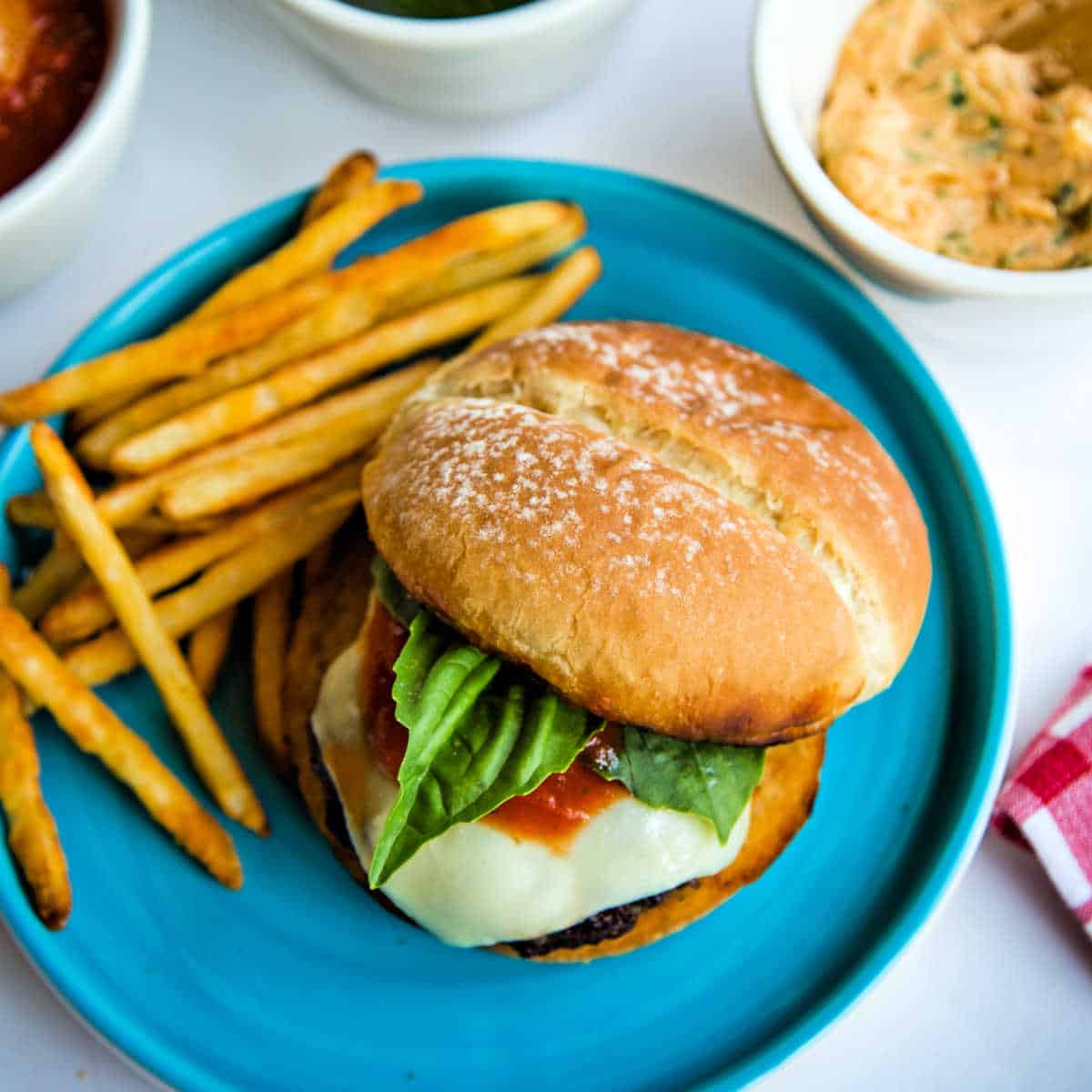 Italian Burgers with Fresh Basil & Roasted Garlic Butter on a blue plate with french fries