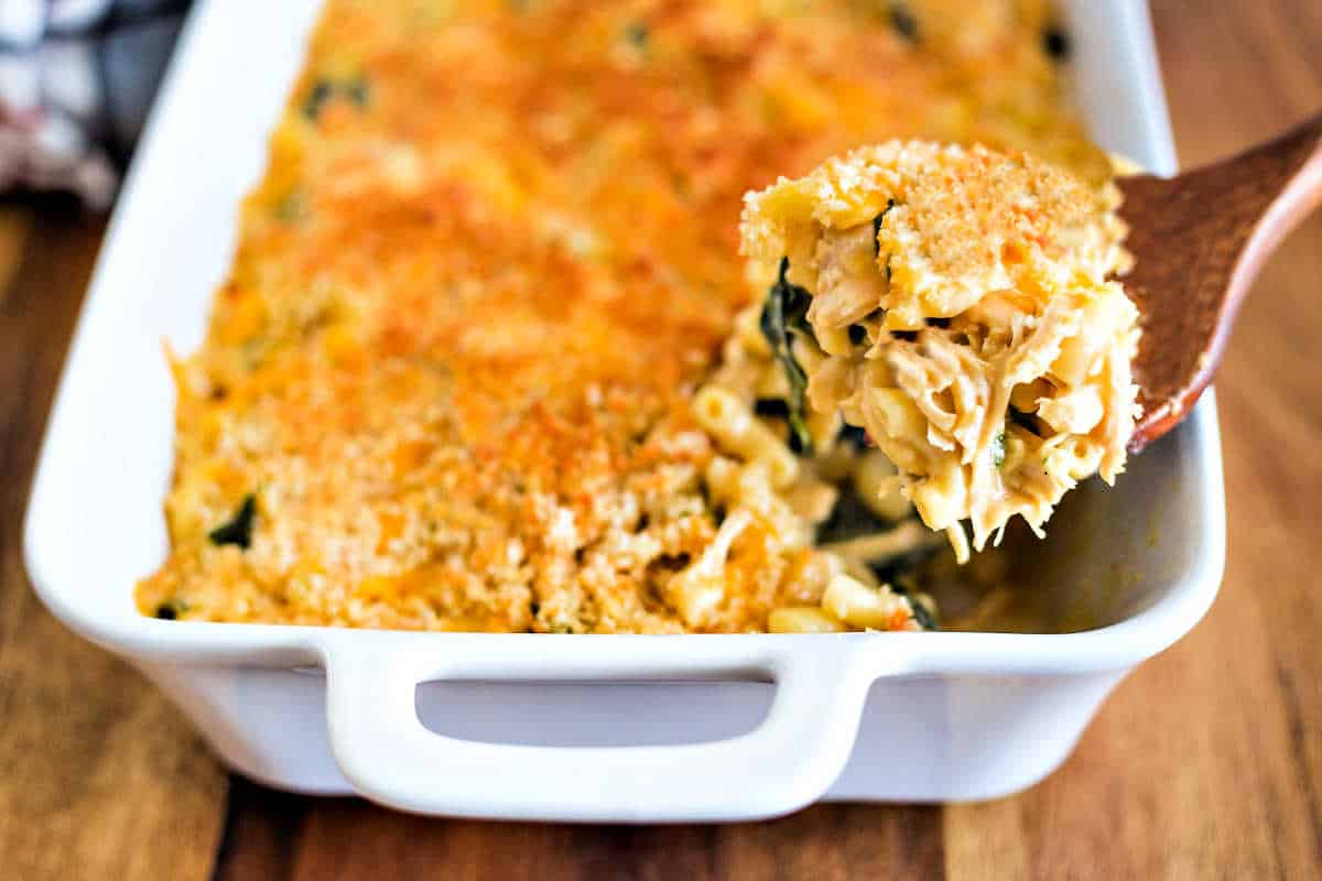 macaroni and cheese casserole in a white baking dish with a wooden spoon