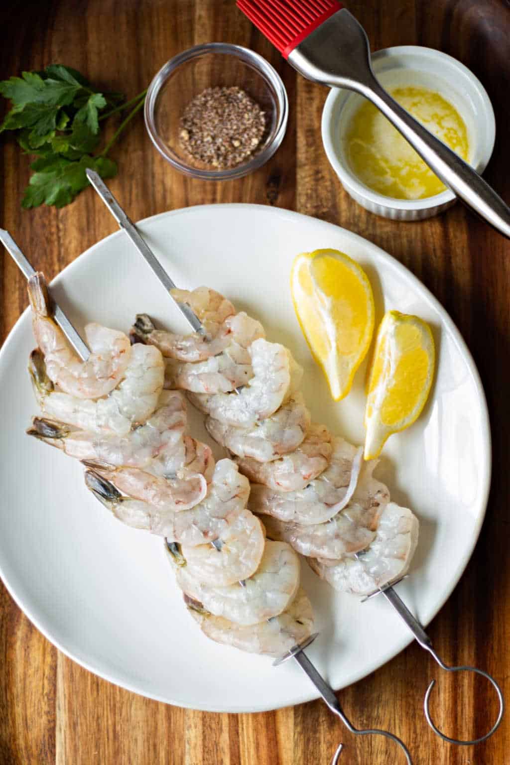 raw shrimp on skewers on a white plate with lemon slces