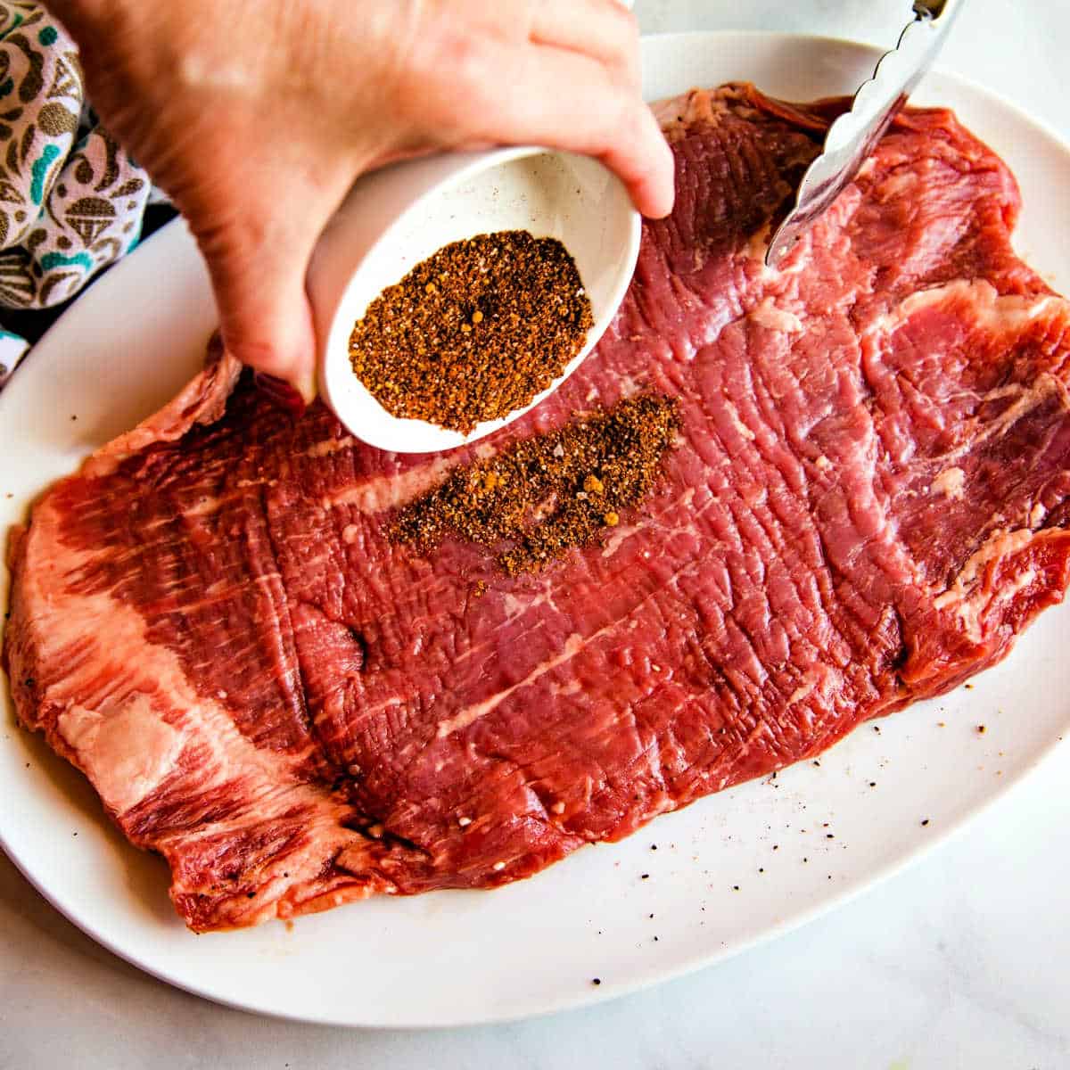 sprinkling dry rub on a flank steak