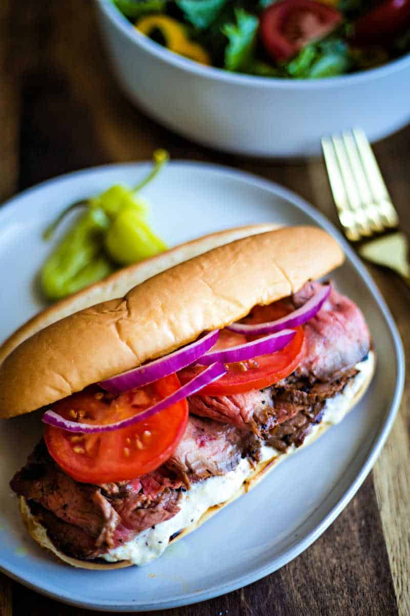 steak sandwich built on a hoagie bun with tomatoes  and red onions 