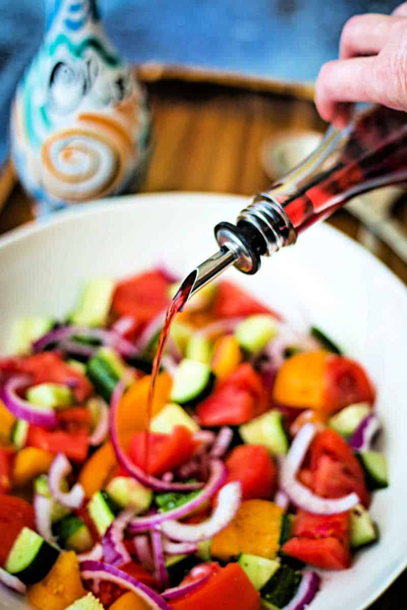 adding red wine vinegar to cucumber tomato feta salad