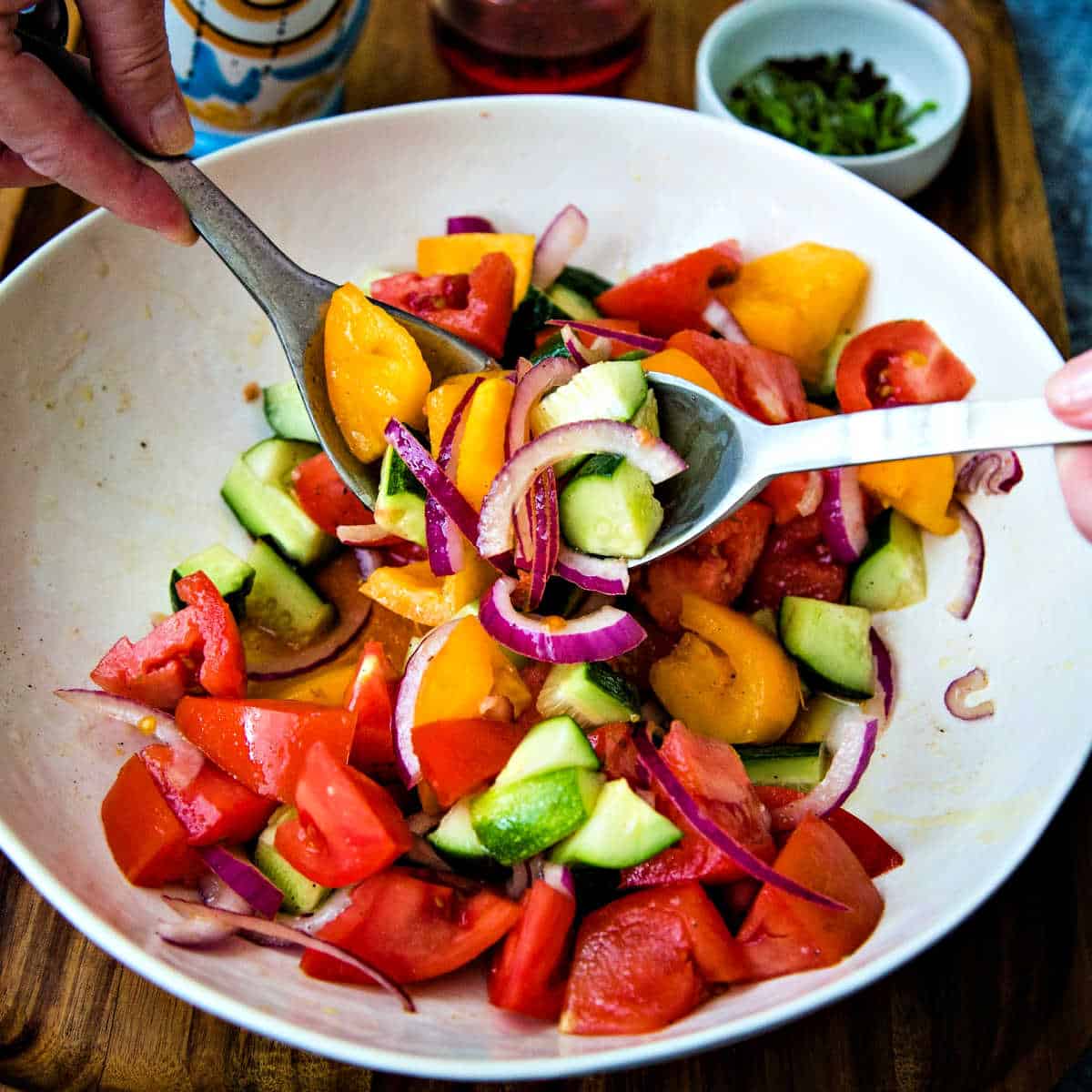 tossing ingredients for cucumber tomato feta salad