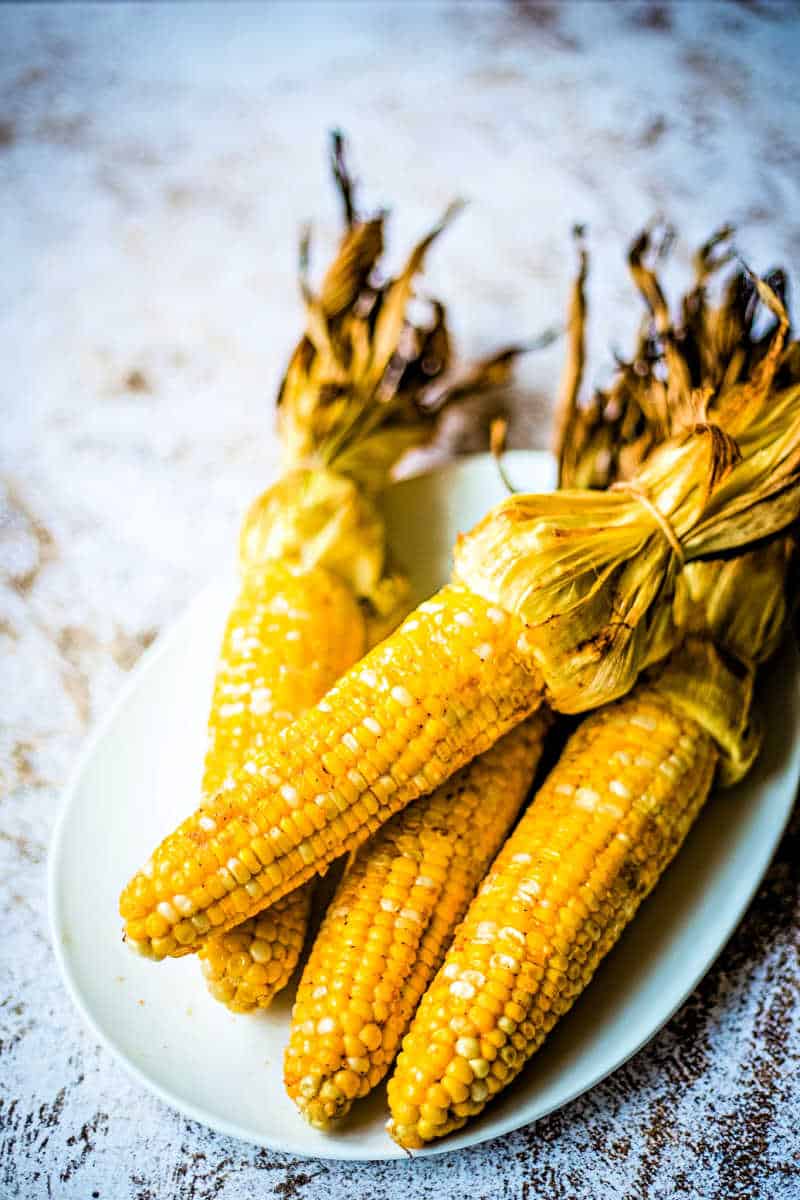grilled corn in husk on a white plate