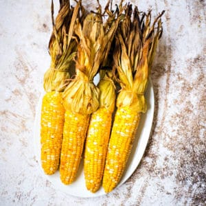 grilled corn in husk on a white platter