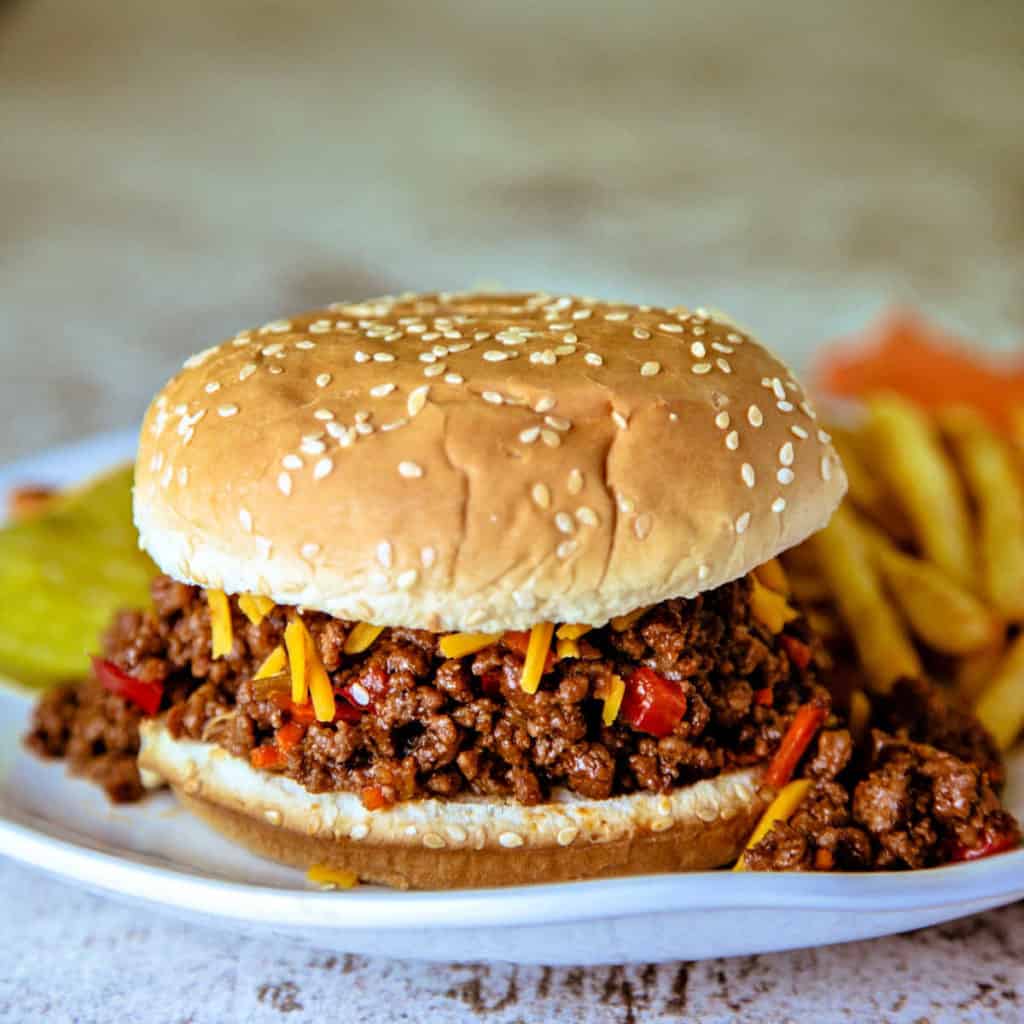 Sloppy Joe Sandwich on a white plate with french fries and topped with cheddar cheese and dill pickles