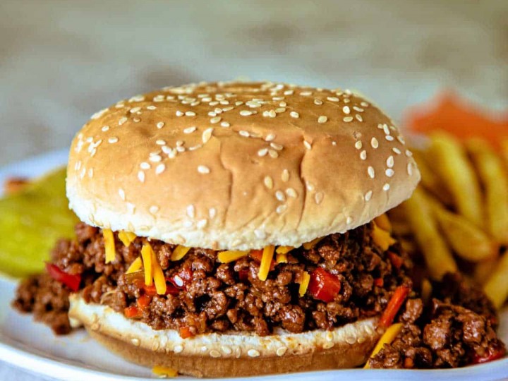 Sloppy Joe Sandwich on a white plate with french fries and topped with cheddar cheese and dill pickles