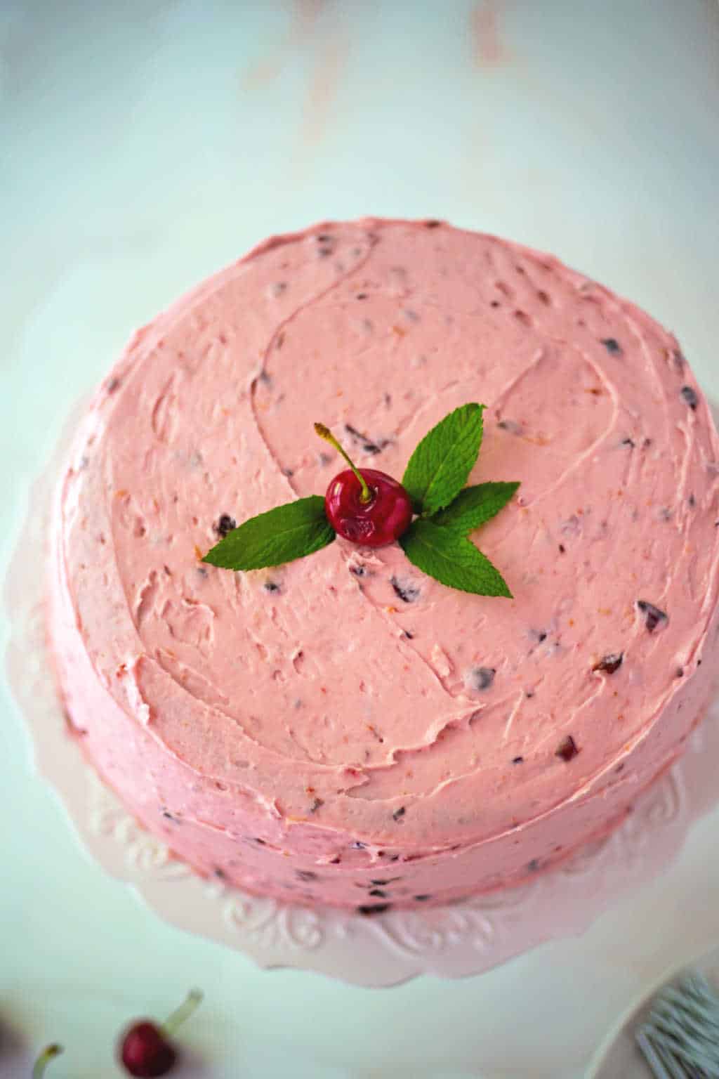 fresh cherry cake with fresh mint and buttercream frosting on a white cake stand