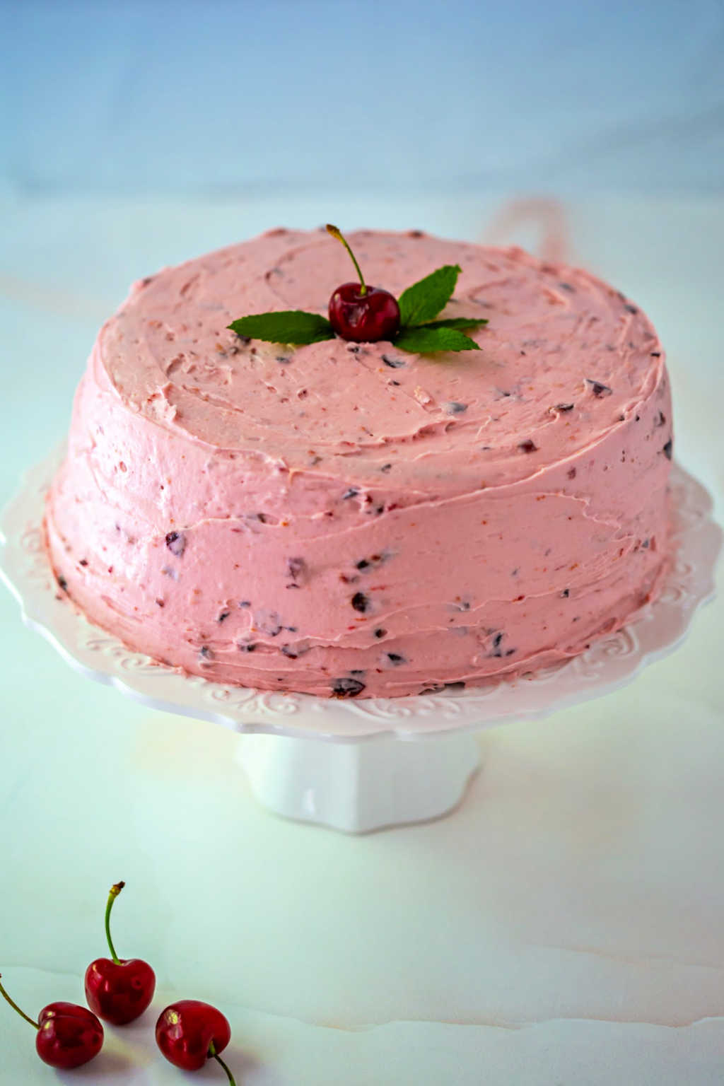 fresh cherry cake with fresh mint and buttercream frosting on a white cake stand
