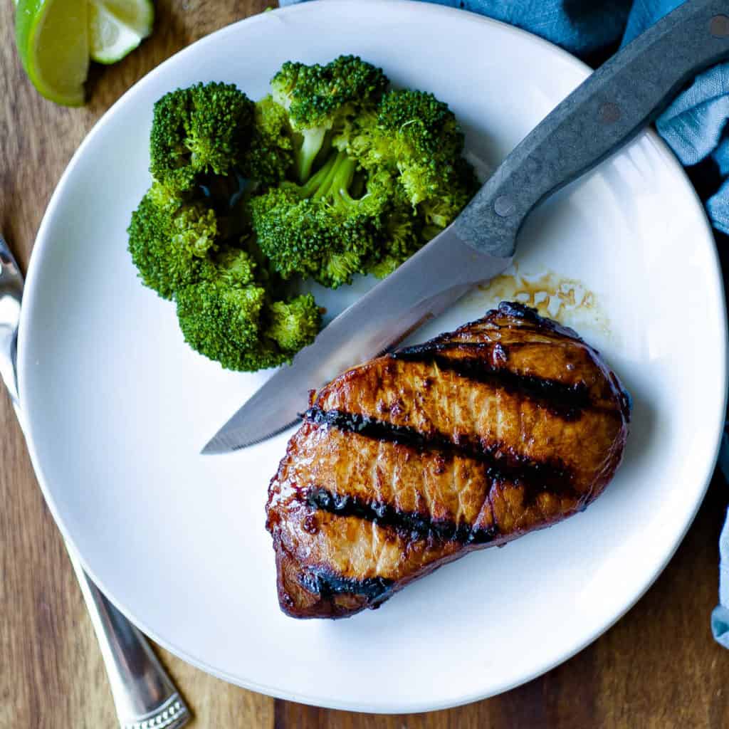 grilled pork chop on white plate with steak knife and broccoli