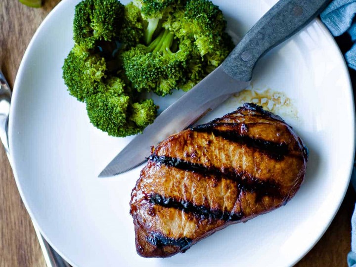 grilled pork chop on white plate with steak knife and broccoli