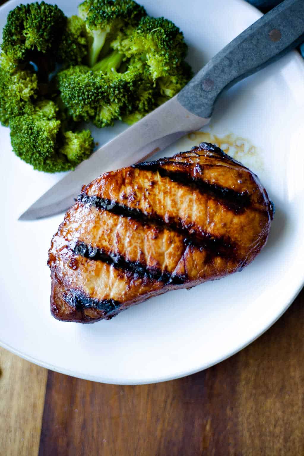 grilled pork chop on white plate with steak knife and broccoli