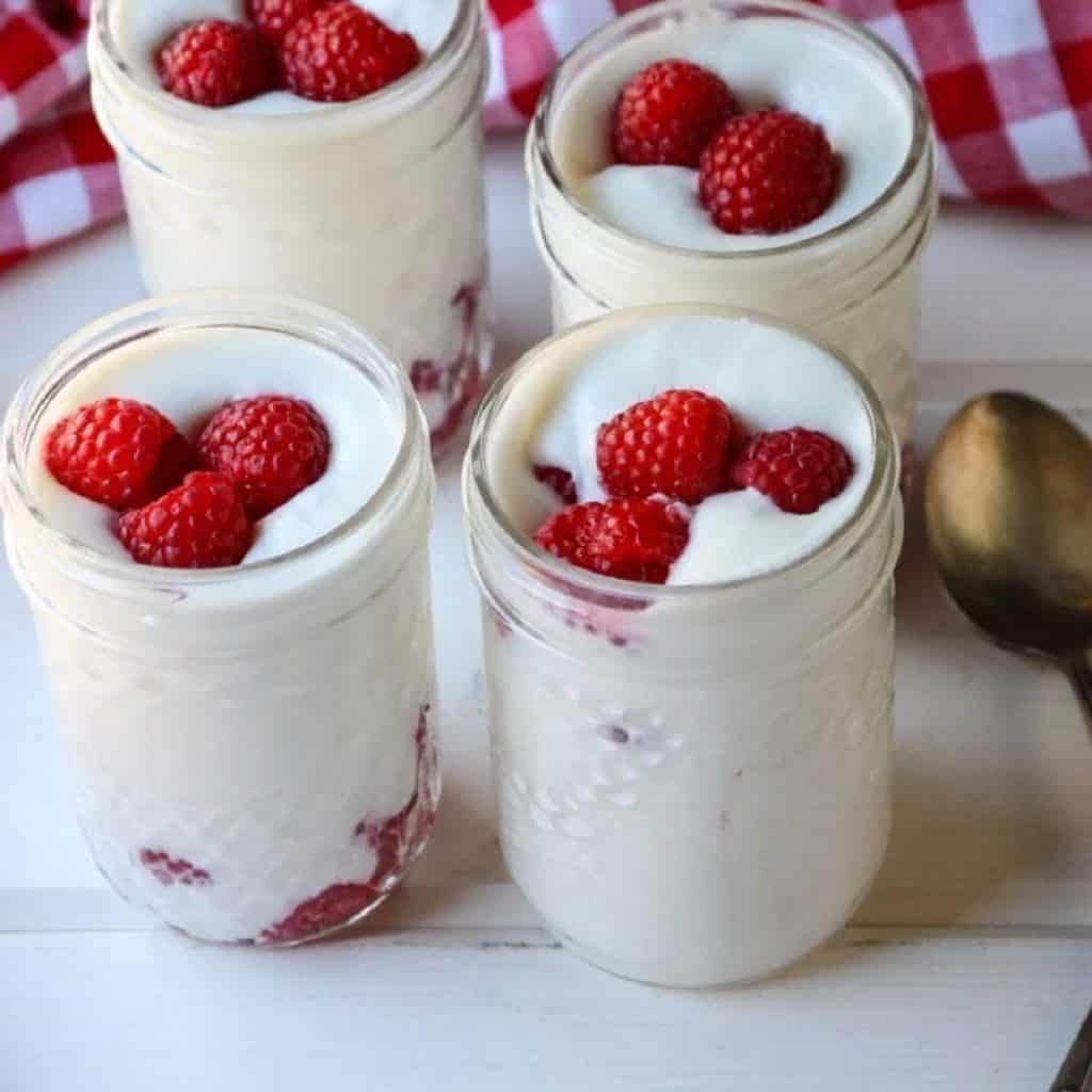 Coconut mousse in jars with raspberries on a table.