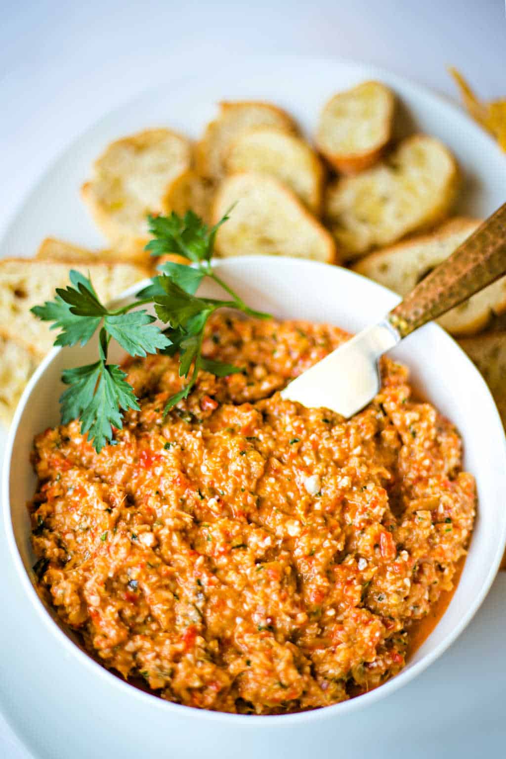 roasted red pepper artichoke tapenade iin a white bowl with baguette slices and fresh parsley