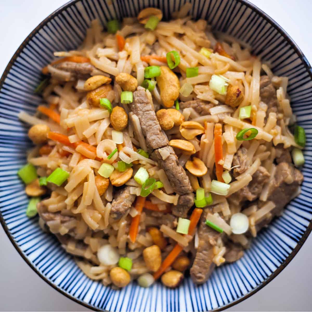 beef pad thai in a blue striped bowl